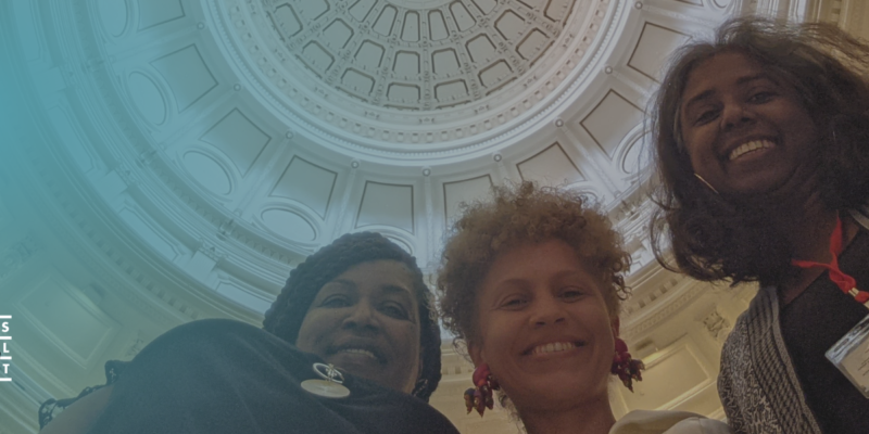 Three women of Texas Jail Project are looking down at the camera. Above is the rotunda of the Texas State Capitol.