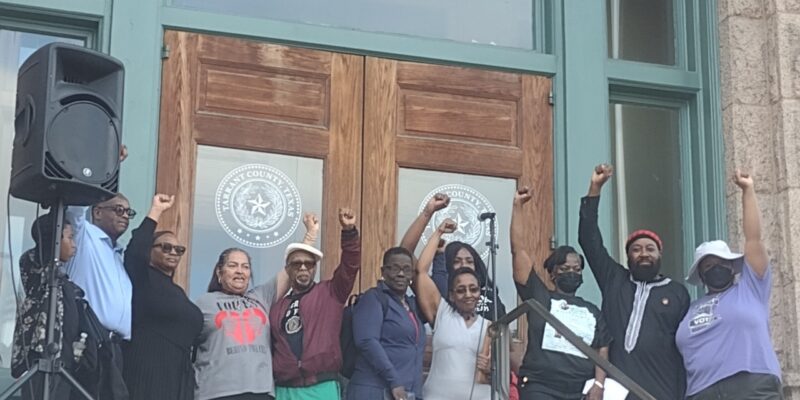 Community members stand with their fists raised in front of the Tarrant County Courthouse